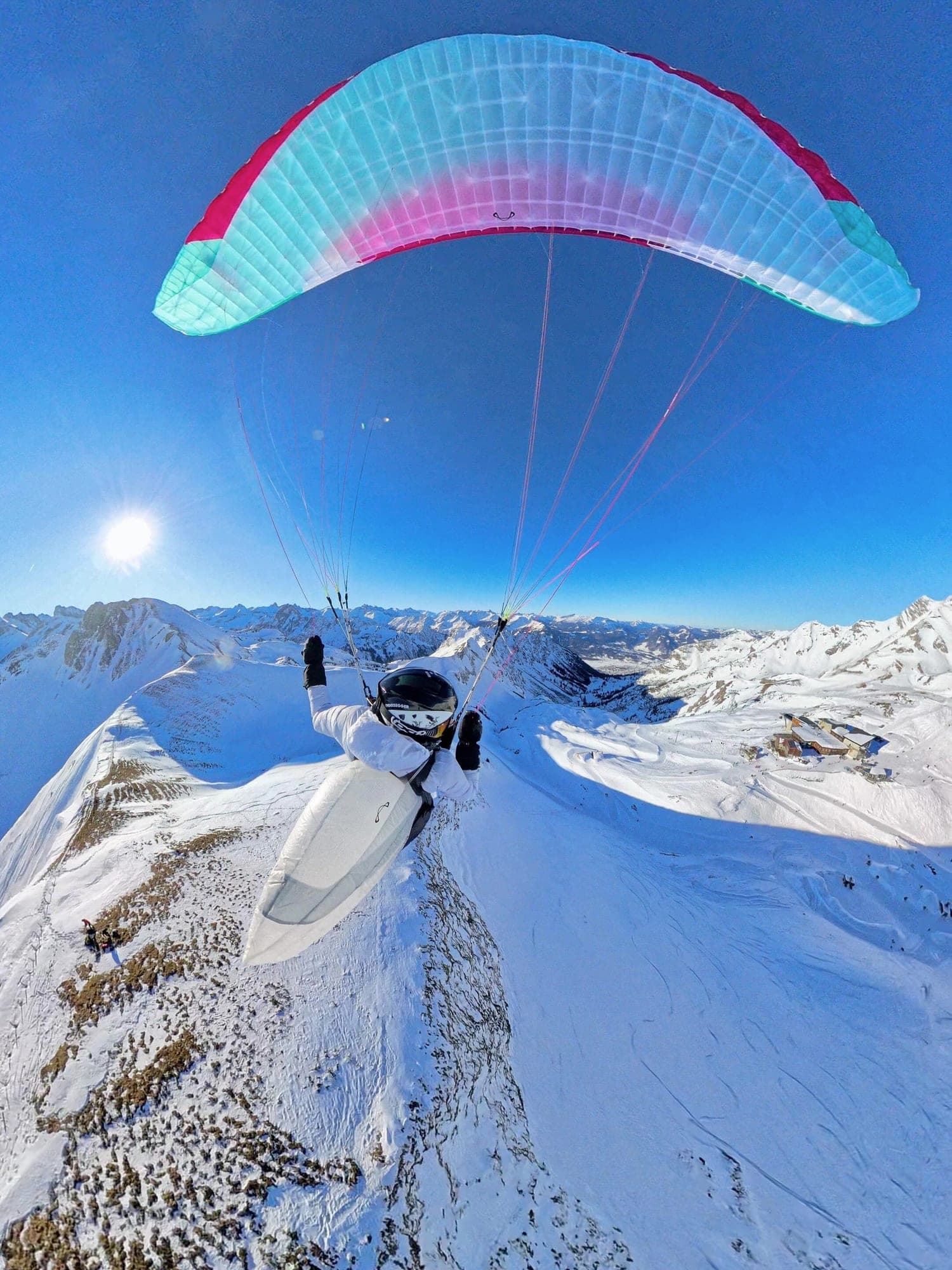 Blick von hinten über einen Tandem-Gleitschirm, der über einem verschneiten Grat abhebt, dahinter die Allgäuer Kette